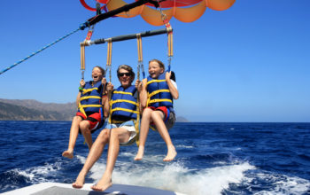 Father and Twin Daughters Parasailing Against a Blue Summer Sky.